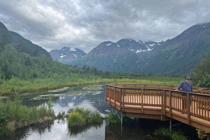 Scenic view of mountains, wooden deck, and calm water with cloudy sky.