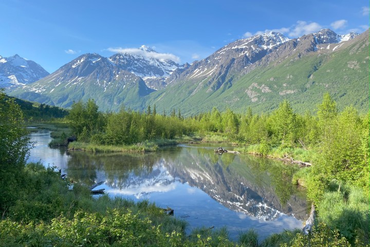 Mountain landscape with a lake, trees, and snow-capped peaks.